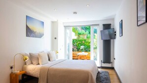 Un dormitorio con cama, mesita de noche, lámpara, televisor y vistas a un jardín a través de un ventanal.