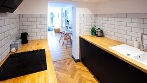 Una cocina moderna con piso de madera en patrón de espiga, estufa por inducción negra, pileta blanca y un mueble negro.