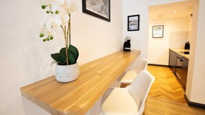 Una cocina moderna con encimera de madera, sillas blancas, una planta en maceta e imágenes enmarcadas en la pared.