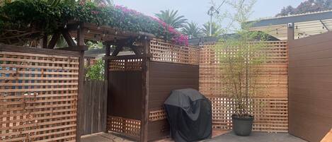 Een omheinde achtertuin met een houten pergola, een overdekte barbecue en een plant in pot.