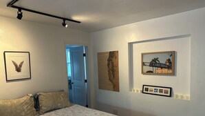 Un dormitorio con una cama, una puerta y obras de arte en la pared, incluyendo un mapa y un cuadro enmarcado.