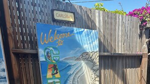 Un portón de madera con un cartel de bienvenida, un tanque de agua y una cerca de madera.