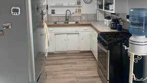 Una cocina moderna con armarios blancos, un refrigerador de acero inoxidable, un lavamanos y una estufa. Hay un dispensador de agua y una jarra de agua grande en la encimera.