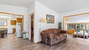 A spacious living area with a brown sofa, wooden flooring, a dining table, and a kitchen visible through an open doorway. - Montana Missouri River Fly Fishing Lodge -3BR & 2 bath, Sleeps 8 (Cascade)