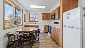 A kitchen with wooden cabinets, a white refrigerator, and a dining table with chairs. - Montana Missouri River Fly Fishing Lodge -3BR & 2 bath, Sleeps 8 (Cascade)