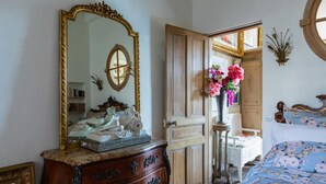 Un dormitorio con un espejo grande y ornamentado, un aparador con cajones, una mesita de noche con un florero y una cama con ropa de cama floral.