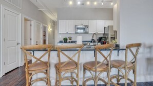 Une cuisine avec des meubles blancs, un four à micro-ondes en acier inoxydable et un coin bar équipé de trois chaises en bois.
