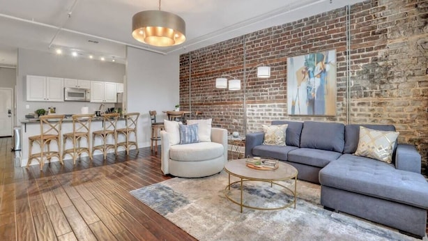 Un salon moderne avec un mur en briques, un canapé, une table basse et un coin repas comprenant des chaises et une table.