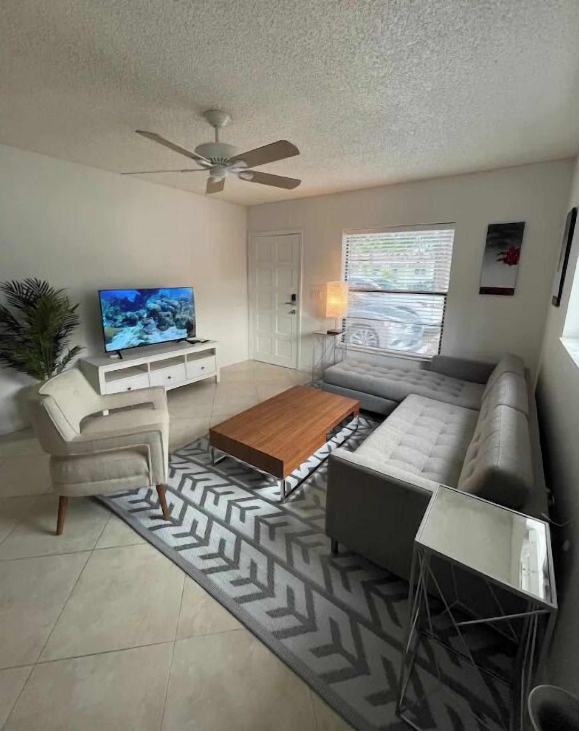 A living room with a television, sofa, coffee table, and a ceiling fan.