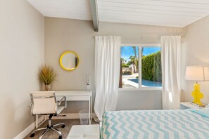 A bedroom with a bed, a desk, a chair, a mirror, a window with curtains, and a view of the outdoors.