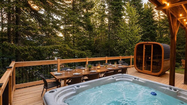 Un bain à remous sur une terrasse en bois, avec une table dressée pour le repas, le tout entouré d’arbres.