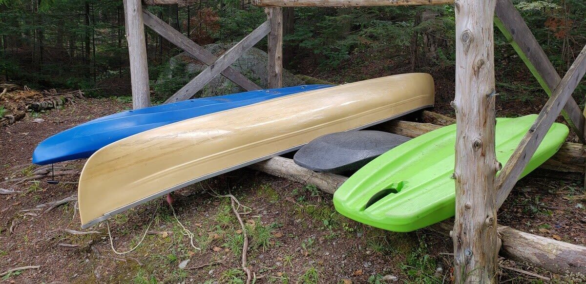 Eine Holzkonstruktion mit drei Kanus: blau, beige und grün.