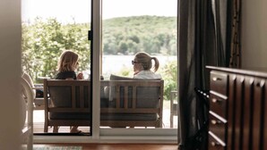 Two people seated on a wooden bench facing a large glass door with a view of a lake and greenery. - Lakeside Chalet, Sauna, Mont Orford & Village (Eastman)