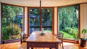 Un comedor con una mesa de madera y bancos, amplias ventanas con vista a follaje y árboles.