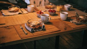 Ein Esstisch mit verschiedenen Speisen und Getränken, eine hängende Leuchte und ein gemütlicher Sitzbereich im Hintergrund.