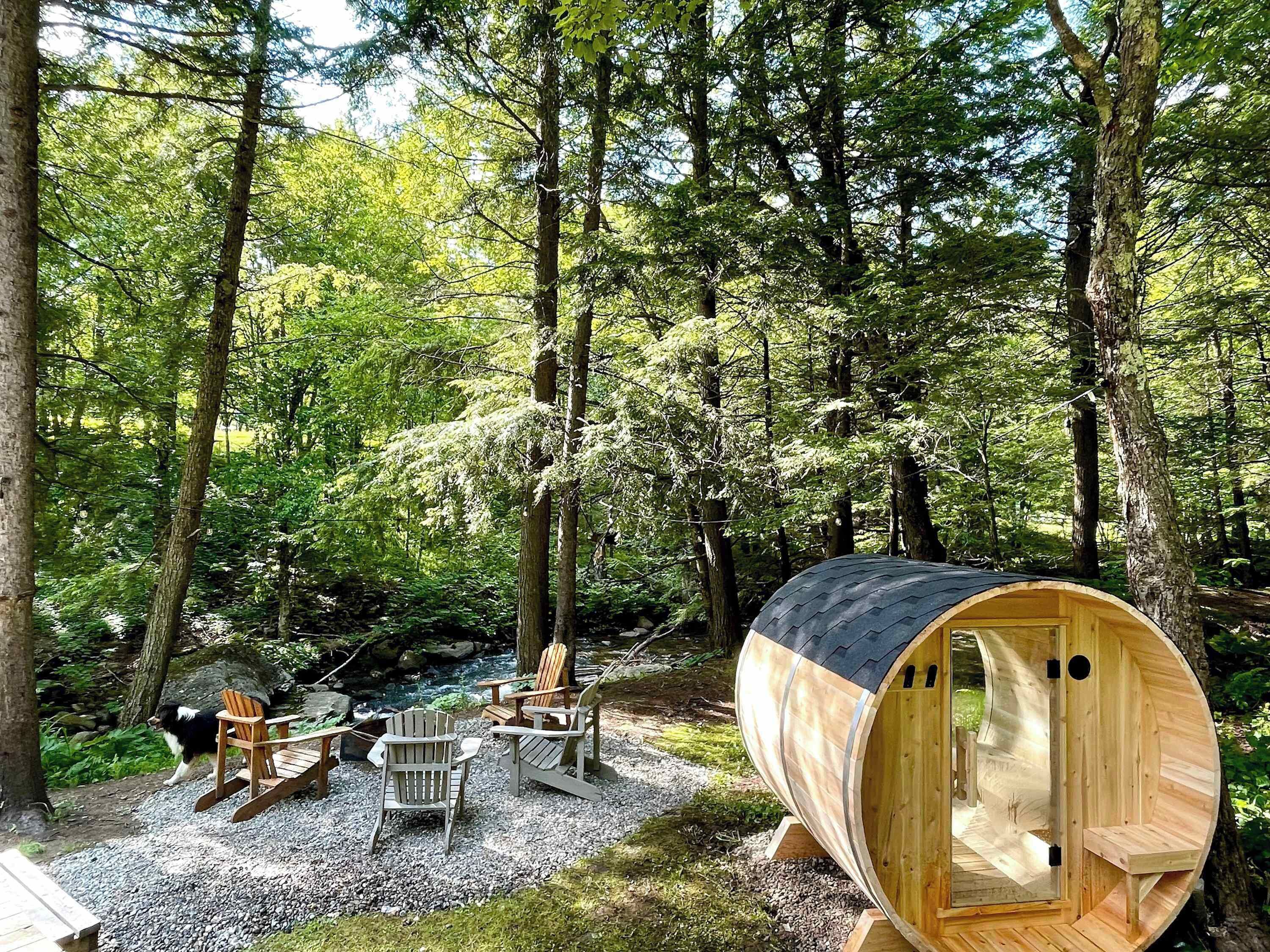 A wooden log cabin with a curved roof, surrounded by a forest. Inside, there are two wooden chairs and a table.