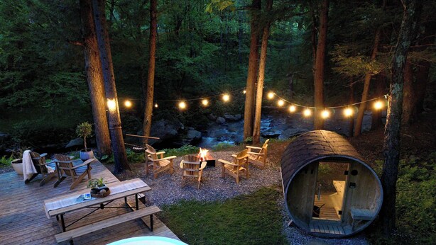 Ein gemütliches Outdoor-Ambiente mit Whirlpool, Holzterrasse, Stühlen und einer Blockhütte.