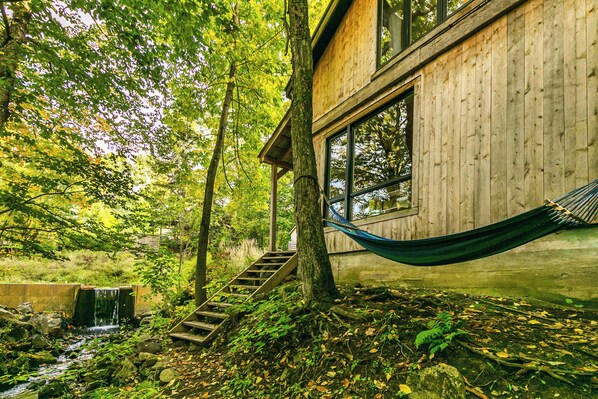 Eine Holzhütte mit großem Fenster, einer Hängematte und einem kleinen Wasserfall.