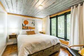 Ein Schlafzimmer mit einem großen Bett, einem Holzkopfteil, einem Nachttisch mit Lampe, einem Fenster mit Vorhängen und einem Bild an der Wand.