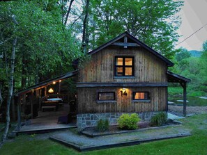 Eine rustikale Holzhütte mit Stein Fundament, einer Veranda und einem beleuchteten Innenraum.