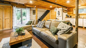 A cozy living room with a leather sofa, wooden ceiling, and a staircase leading to a kitchen.
