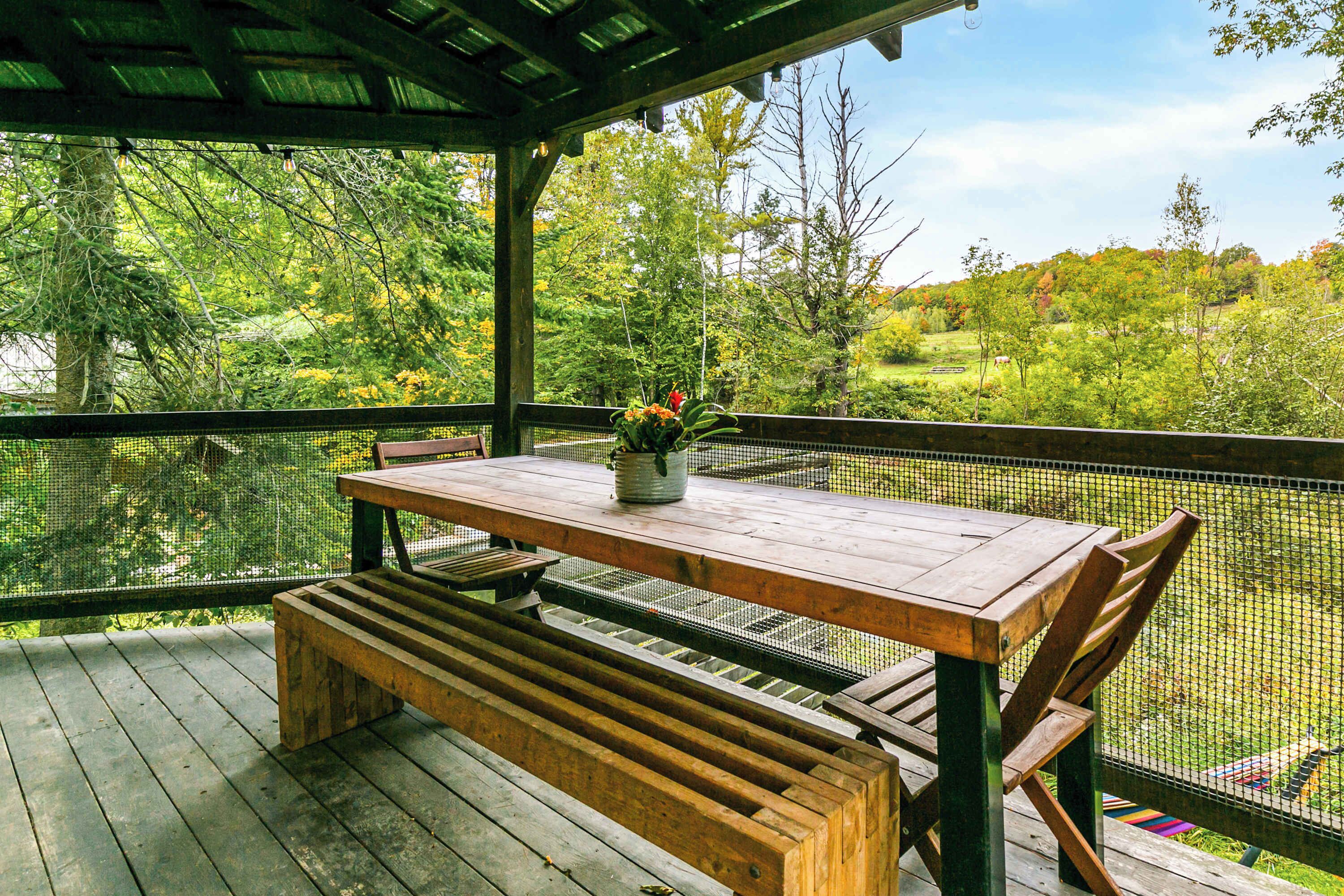 A wooden deck with a table and bench, surrounded by a mesh fence, overlooking a natural landscape.