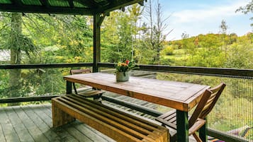 A wooden deck with a table and bench, surrounded by a mesh fence, overlooking a natural landscape.