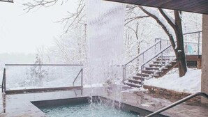 Ett bubbelbad med en vattenfallsfunktion, omgivet av snötäckta trappor och träd.