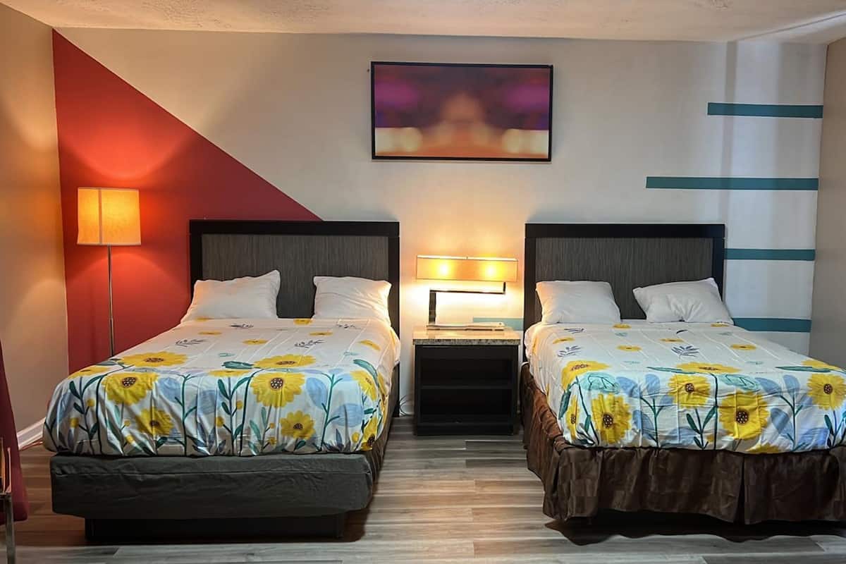 A hotel room with two beds, each with a floral bedspread, a nightstand with a lamp, and a painting on the wall.