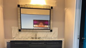Een moderne badkamer met een marmeren wastafel, een grote spiegel en een inbouwlamp.