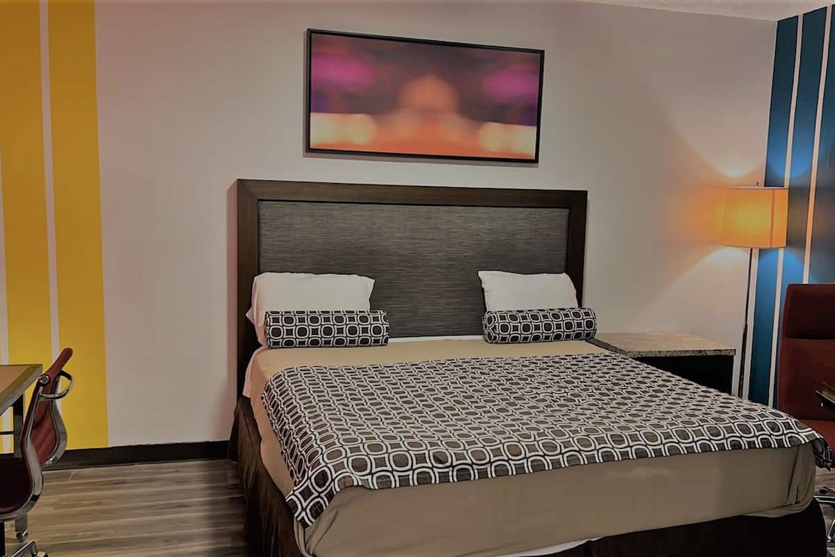 A hotel room with a bed, a desk, a chair, and a lamp.