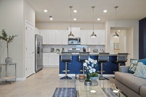 Cocina moderna con armarios blancos, refrigerador de acero inoxidable, microondas e isla azul con taburetes de bar.