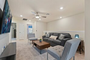 A modern living room with a grey sofa, a grey armchair, a wooden coffee table, and a television. - 5-bedroom townhome with a screened plunge pool at Solterra Resort, near Disney (Davenport)
