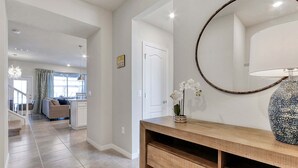 Ein modernes Interieur mit einem Holzkonsolentisch, einem runden Spiegel und einer Vase mit weißen Blumen.