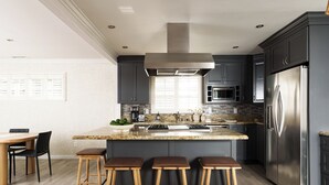 Una cocina moderna con armarios oscuros, electrodomésticos de acero inoxidable y una isla central con taburetes.