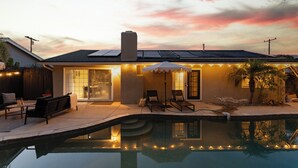 Una casa con piscina, mobiliario de exterior y paneles solares en el techo.