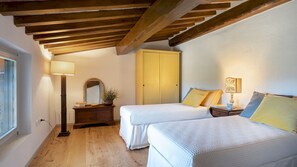 Une chambre avec deux lits, un plafond en bois, une armoire et une table de chevet avec une lampe.
