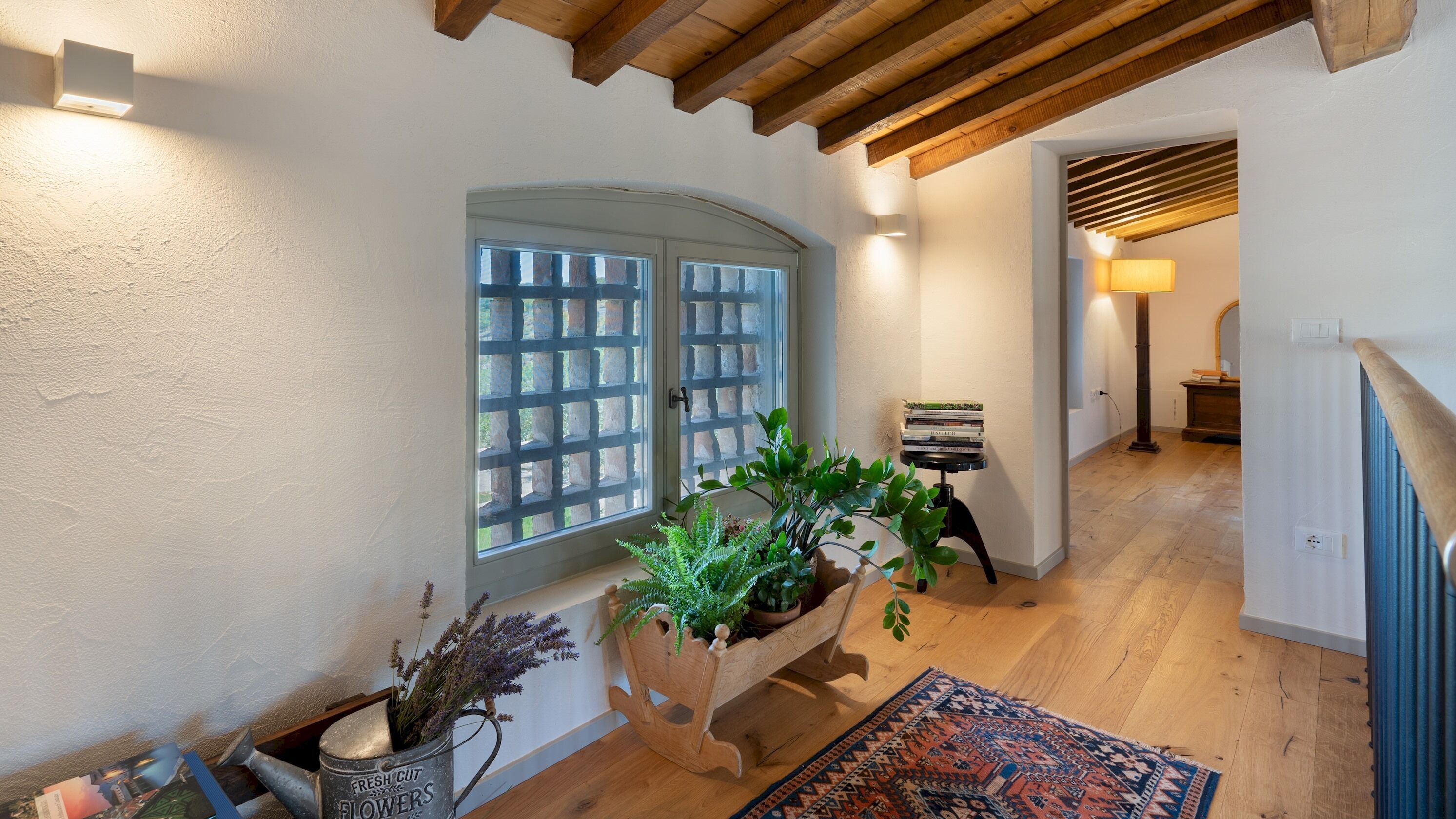 Un pasillo con piso de madera, un tapete estampado, un banco de madera con plantas y una puerta con paneles de vidrio esmerilado.
