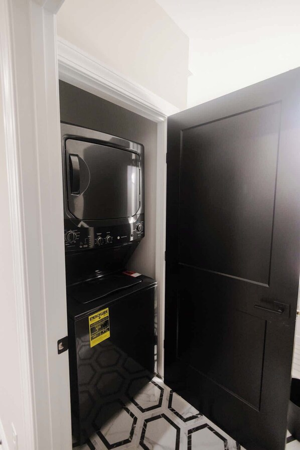 Una habitación compacta con lavadora y secadora integradas, una puerta negra y un suelo estampado.