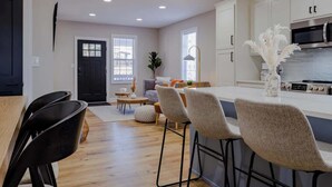 Una cocina moderna con armarios blancos, una estufa de acero inoxidable y un comedor con mesa de madera y sillas negras.