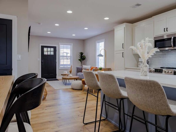 Una cocina moderna con armarios blancos, una estufa de acero inoxidable y un comedor con mesa de madera y sillas negras.