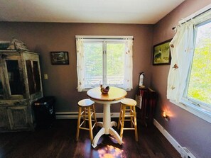 Un comedor con una mesa redonda y dos taburetes, una ventana con cortinas y un radiador.