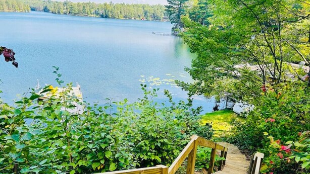 A wooden staircase leading to a lakeside area with lush greenery and a view of a calm lake. - Waterfront Splendor in the Woods. (Florence)