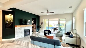 A modern living room with a fireplace, a sofa, a coffee table, and a TV mounted on the wall. - Chimayo House with Pool and Spa near Palm Springs - Sleep 6 (Cathedral City)