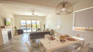 A spacious living area with a white dining table, modern chairs, and a large window overlooking a pool. - Chimayo House with Pool and Spa near Palm Springs - Sleep 6 (Cathedral City)