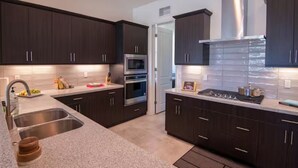 A modern kitchen with dark cabinets, stainless steel appliances, and a large island with a sink. - Chimayo House with Pool and Spa near Palm Springs - Sleep 6 (Cathedral City)