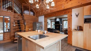 Interior de una cabaña de madera con cocina, comedor y una escalera.