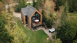 A modern cabin with a large deck, surrounded by dense forest. - Nômade - Spa, private lake access & stunning views (Chertsey)