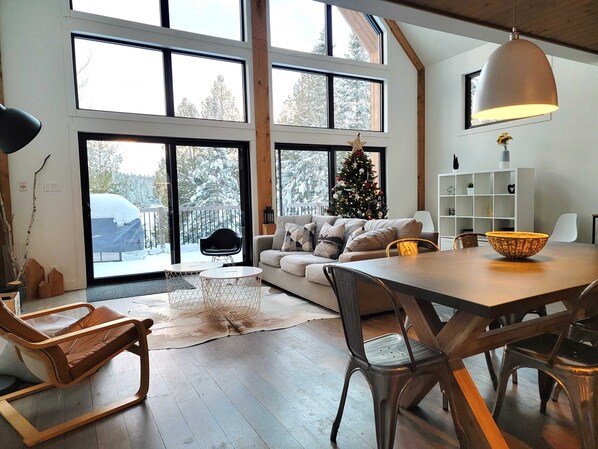A spacious living room with a large window, a Christmas tree, a dining table, and a cozy seating area.