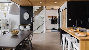 A modern kitchen with a wooden ceiling, a dining area with a large table, and a staircase leading to another level. - Nômade - Spa, private lake access & stunning views (Chertsey)